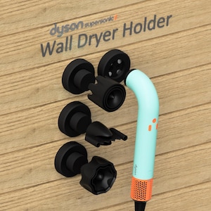 May include: A wall-mounted holder for a Dyson Supersonic hair dryer. The holder is black and has a round base. The hair dryer is light blue and has a black handle. The text "Dyson Supersonic" and "Wall Dryer Holder" is visible on the wall.