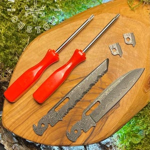 以下が含まれることがあります： ダマスカス鋼の刃、赤いハンドル付きのドライバー2本、小さな金属片2つを含むツールセット。ツールは緑の苔を背景にした木製の表面に配置されています。ツールには「Forge & Bone Custom Est. 2024」のラベルが貼られています。