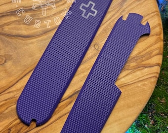 May include: Two purple textured knife handle scales with a cross symbol and the text "FORGE & BONE CUSTOM" on a wooden surface. The scales are designed to fit a knife and have a textured surface for grip.
