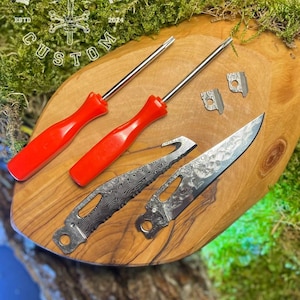 Op de afbeelding: Op maat gemaakte gereedschappen gerangschikt op een houten oppervlak. De afbeelding toont twee schroevendraaiers met rode handvatten, twee metalen onderdelen en twee messen met patronen op de bladen. Het logo "FORGEBONE CUSTOM" is zichtbaar.