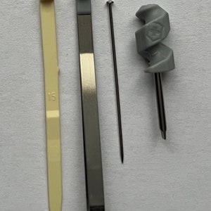 May include: A set of three tools for crafting or repairs. The tools include a gray plastic tool with a spiral design, a silver metal tool with a pointed end, and a white plastic tool with a pointed end and the number "13" printed on it.