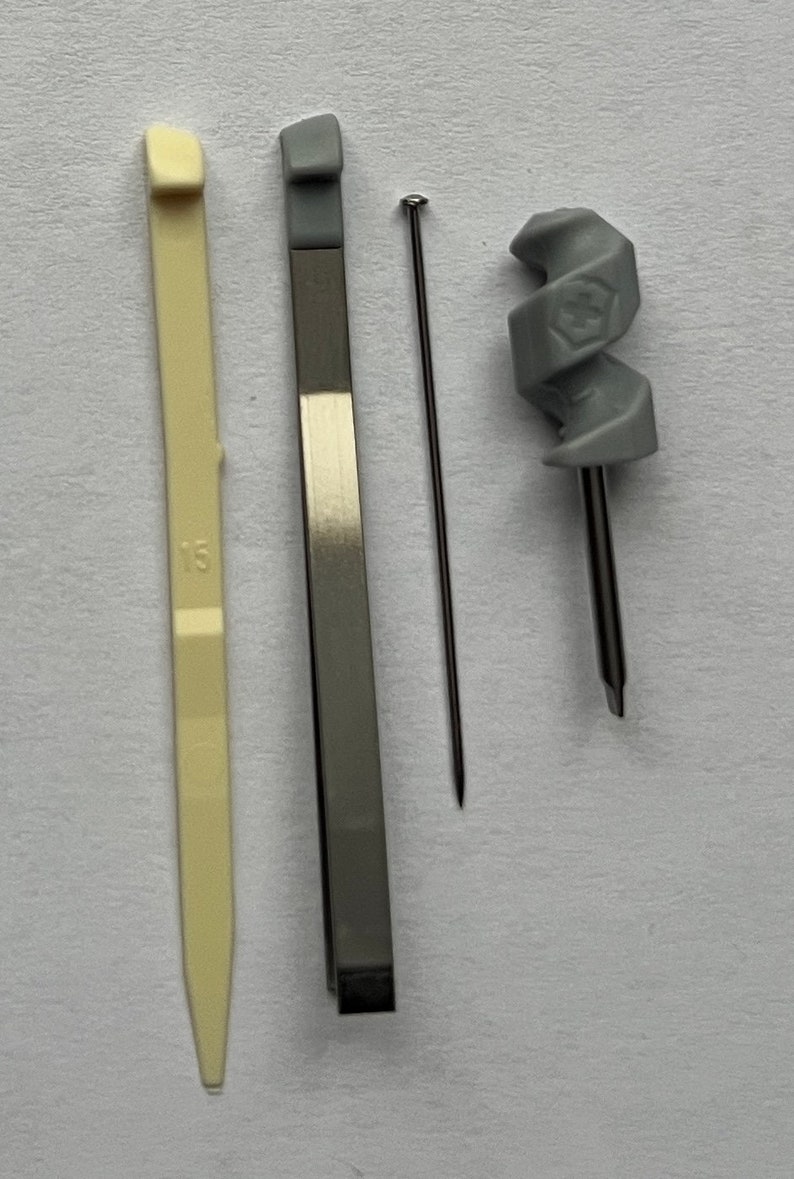 May include: A set of three tools for crafting or repairs. The tools include a gray plastic tool with a spiral design, a silver metal tool with a pointed end, and a white plastic tool with a pointed end and the number "13" printed on it.