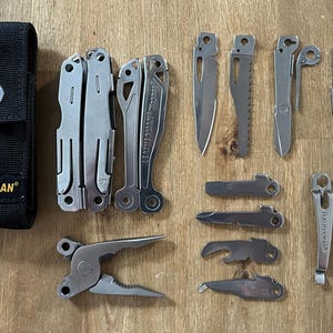 Könnte beinhalten: Ein Set aus silbernen Multitools und Zubehör, darunter ein Leatherman Multitool, eine Leatherman Hülle, ein Flaschenöffner, eine Säge, ein Schraubendreher und ein Satz Schrauben.