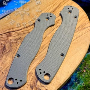 May include: Two grey textured knife handle scales with a cross-hatched pattern, featuring pre-drilled holes for assembly. A logo with the text FORGEBONE CUSTOM ESTD 2024 is visible in the upper left corner, depicting a hammer and crossed bones.