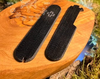 May include: Two black textured knife handle scales with a white cross emblem, displayed on a wooden surface. The scales are custom-made, as indicated by the text "CUSTOM" and "FORGE&BONE" in the background.