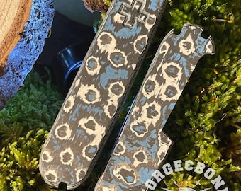 Könnte beinhalten: Zwei blaue und weiße gemusterte Schalen für ein Schweizer Taschenmesser. Die Schalen haben ein weißes Kreuz auf der oberen Schale und den Text "FORGECBONE ESTD 2024 CUSTOM" auf der unteren Schale.