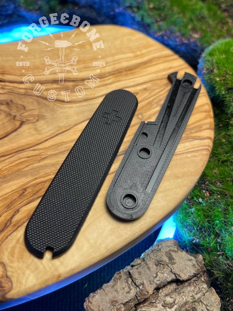 May include: Two black custom parts, one rectangular with a textured surface and the other with a unique shape. The parts are displayed on a wooden surface with the "Forge & Bone Custom" logo. The logo includes the text "ESTD 2024".