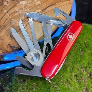 Könnte beinhalten: Ein rotes Multitool-Messer mit verschiedenen Edelstahlwerkzeugen, darunter eine Säge, eine Schere und ein Flaschenöffner. Das Messer hat ein weißes Kreuzemblem. Das Messer liegt auf einer Holzoberfläche mit dem Text "FORGE&BONE CUSTOM" und dem Jahr "2024".