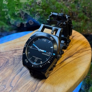May include: A black Leatherman wristwatch with a black dial, white numerals, and bright blue accents on the hands and markers. The watch features a Swiss movement, a rotating bezel with white markings, and a multi-link black metal bracelet band.
