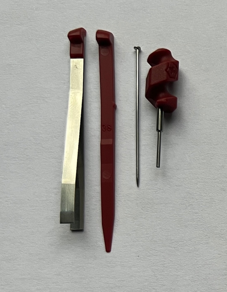 May include: A set of three tools for watch repair. The tools are made of metal and plastic and are red and silver in color. The tools include a pair of tweezers, a small screwdriver, and a tool with a pointed end.