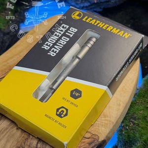 Könnte beinhalten: Ein Leatherman Bit Driver Extender in der Originalverpackung. Die Schachtel ist gelb und schwarz, mit dem Leatherman-Logo und Produktinformationen. Der Extender ist silberfarben und durch ein transparentes Fenster sichtbar. Die Box weist auch darauf hin, dass es sich um einen 1/4" Sechskant-Bit-Treiber mit einem magnetischen Bithalter handelt.