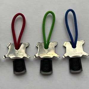 Op de afbeelding: Vijf zilveren sleutelhangers met verschillende gekleurde koorden. Elke sleutelhanger heeft een klein gereedschap met de gravure "VICTORINOX".