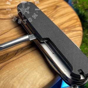 May include: A multi-tool with a textured black handle and a silver metal body. The tool includes various implements and a key ring attachment. The text "FORGE & BONE CUSTOM" is printed on the handle.