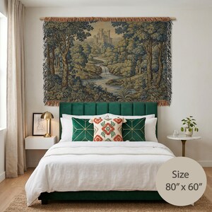 May include: A woven wall tapestry featuring a landscape scene with a castle, a river, and trees in shades of blue, green, and tan. The rectangular textile has fringed edges and measures 80 inches by 60 inches as indicated on the product label.