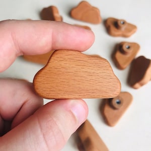 May include: A set of wooden cloud-shaped drawer pulls in a light brown colour. The pulls have a smooth, slightly textured surface and are designed to be used as cabinet hardware.