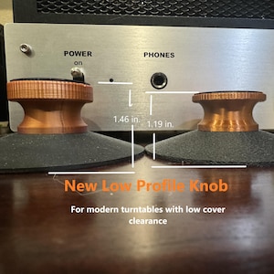 May include: Two copper-colored turntable knobs with black bases. The knobs are 1.46 inches and 1.19 inches tall. The text "New Low Profile Knob" and "For modern turntables with low cover clearance" is below the knobs.