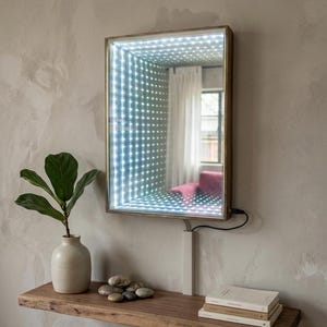 May include: Rectangular LED infinity mirror with a gold frame, mounted on a wall. The mirror reflects a grid of lights, creating a depth illusion. A wooden shelf below holds a vase with a plant, stones, and books.