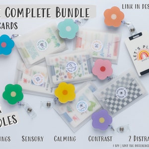 May include: A set of six colourful flower-shaped lanyards with clear plastic pouches containing 30 cards. The pouches are labelled with the words "Feelings", "Sensory", "Calming", "Contrast", and "2 Distraction". The text "Let's Play" is visible on a black card with a rainbow design.