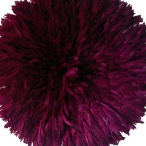 May include: A circular wall decoration composed of dark burgundy feathers. The feathers are closely arranged, forming a textured, spherical shape. The wall decor is set against a white backdrop.