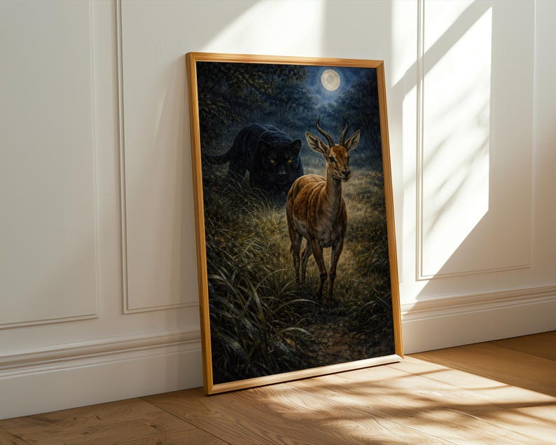 May include: A framed art print depicts a deer in a grassy field under a full moon, with a black panther lurking in the background. The artwork is set in a wooden frame and leans against a white wall.