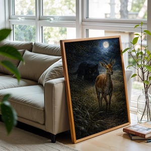 May include: A framed art print featuring a nighttime forest scene with a deer and a black panther. The deer stands in a grassy area, illuminated by moonlight. The artwork is displayed near a window and a beige sofa.