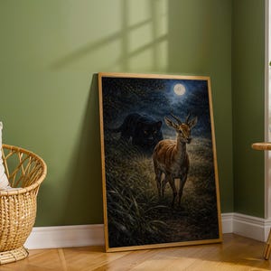 May include: A framed art print depicts a deer in a forest under a full moon, with a black panther in the background. The artwork has a natural color palette and is set in a room with a green wall and a wicker chair.
