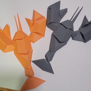 May include: Two geometric sculptures of lobsters. One is orange, the other is gray. The sculptures are made of angular, faceted shapes, giving them a modern, abstract appearance. The lobster claws and tails are clearly defined.