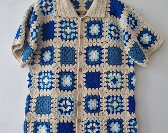 May include: A crocheted button-up shirt with short sleeves. The shirt is made of beige yarn and features a geometric pattern of blue and white squares.