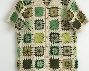 May include: A crocheted button-up shirt with short sleeves. The shirt is made of a cream-colored yarn and features a patchwork design of green, brown, and beige squares.