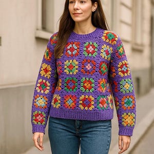 Op de afbeelding: Een paarse gehaakte trui met een kleurrijk granny square patroon. De trui heeft lange mouwen en een ronde hals.