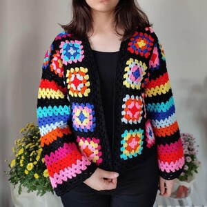 May include: A black crochet cardigan with colorful granny square patterns. The cardigan has a V-neck and long sleeves.