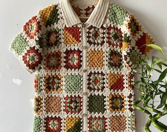 May include: A crocheted button-up shirt with a patchwork design featuring squares in shades of brown, green, orange, and yellow.