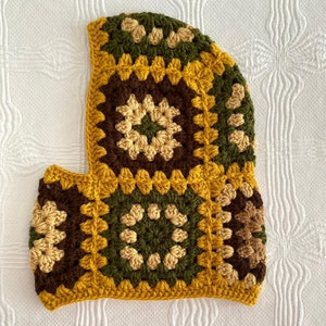 May include: A crocheted hat with a brown, green, and yellow geometric pattern. The hat has a flap that covers the face.