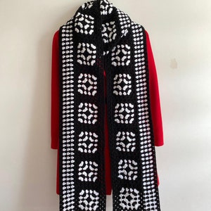 May include: Black and white crocheted scarf with a geometric pattern and black pom-poms on the ends.