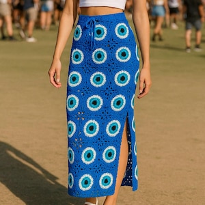 May include: A blue crochet skirt with a repeating eye pattern. The skirt has a high waist with a drawstring and a side slit. The eye pattern features white, black, and light blue details. The skirt is worn with a white crop top and sandals.