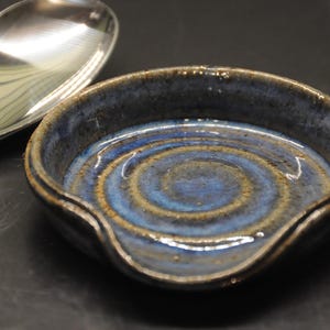 May include: A blue and brown ceramic spoon rest with a wavy edge. The rest has a swirl pattern in the glaze.