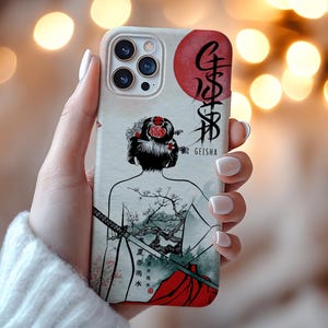 Op de afbeelding: Een telefoonhoesje met een geisha-ontwerp. De hoes heeft een cr&egrave;mekleurige achtergrond met een geisha-illustratie, een rode zon en Japanse tekst. De geisha heeft een bloemenkapsel en een tatoeage van een boom- en berglandschap.