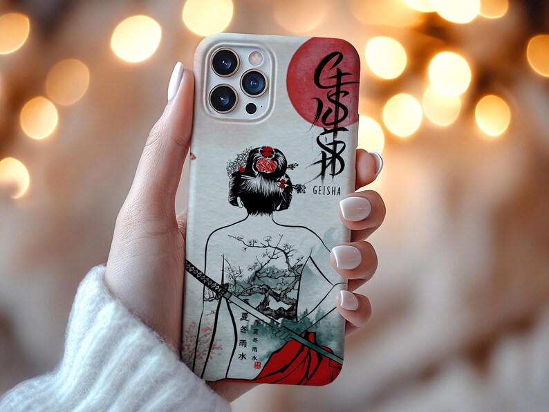 Op de afbeelding: Een telefoonhoesje met een geisha-ontwerp. De hoes heeft een cr&egrave;mekleurige achtergrond met een geisha-illustratie, een rode zon en Japanse tekst. De geisha heeft een bloemenkapsel en een tatoeage van een boom- en berglandschap.