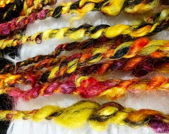 May include: Close-up of colorful yarn strands. The yarn is twisted and features a mix of yellow, orange, red, purple, and black hues. The yarn appears to be soft and textured, suitable for various crafting projects.