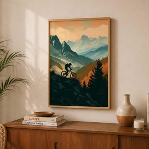 May include: A rectangular wall art print featuring a silhouette of a person riding a mountain bike on a cliff edge. The landscape depicts layered blue mountains, dark green pine trees, and an orange sunset sky with soft clouds in a vertical orientation.