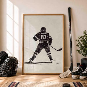 May include: A framed vertical art print featuring a black and white illustration of an ice hockey player from behind, wearing a jersey with the name HENRICH and the number 87, holding a hockey stick while standing on a light-colored background.