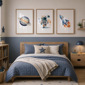 May include: Three framed wall art prints featuring watercolor illustrations of a planet with rings, an astronaut in a space suit, and a rocket ship launching with orange flames, displayed in a row above a wooden bed frame with blue bedding.