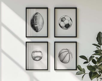 May include: Four framed black and white sports art prints. The prints feature a football, soccer ball, baseball, and basketball. The artwork is a pencil sketch style, with each ball centered in the frame.