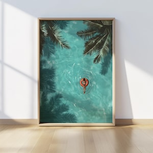 May include: An aerial view of a person floating in a turquoise pool on a red inflatable ring. Palm tree leaves are visible above the water.