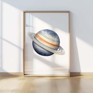 May include: A framed wall art print featuring a watercolor illustration of the planet Saturn. The planet is depicted with shades of deep blue, grey, and orange, surrounded by prominent rings in light beige and white tones, set against a white background.