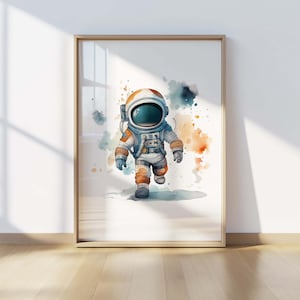 May include: A framed wall art print featuring a watercolor illustration of an astronaut in a white and orange spacesuit with a dark visor, set against a white background with abstract blue and orange paint splatters surrounding the figure.