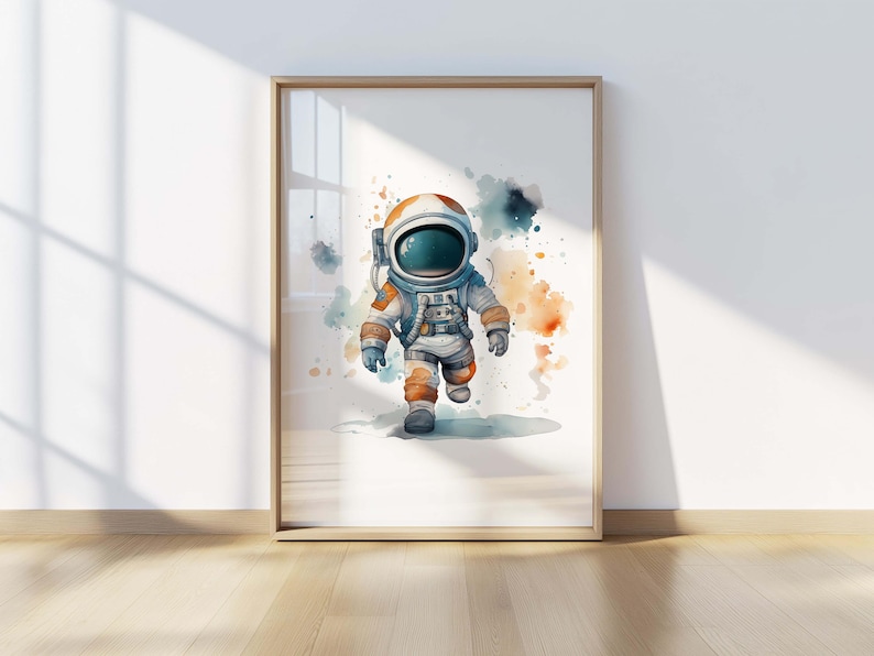 May include: A framed wall art print featuring a watercolor illustration of an astronaut in a white and orange spacesuit with a dark visor, set against a white background with abstract blue and orange paint splatters surrounding the figure.