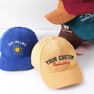 May include: A collection of corduroy baseball caps in various colors, including blue, tan, and burgundy. The caps feature embroidered text and designs, such as "THE JOLLRY" with a sun, "YOUR CUSTOM Embroidery", and "EST. TENNIS CLUB".