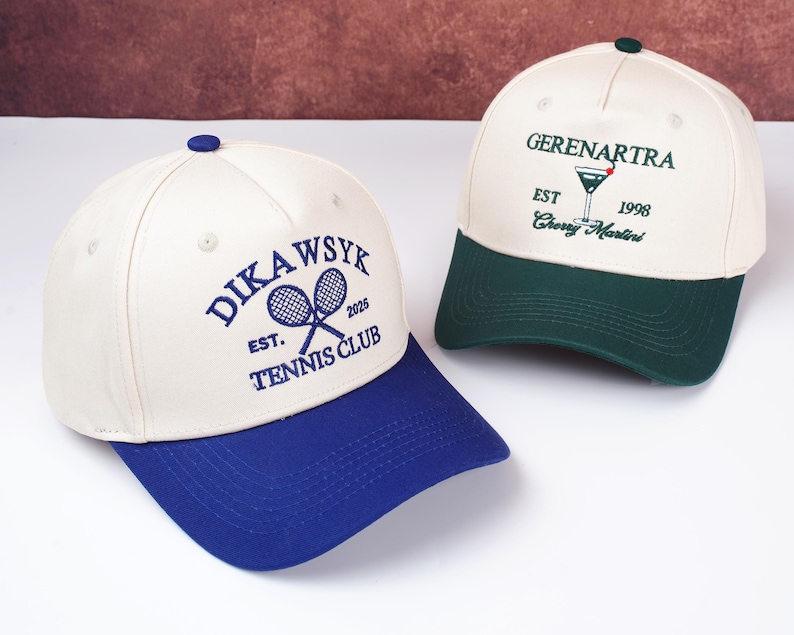 May include: Two baseball caps. One is cream-colored with a blue brim and the text "DIKAWSYK EST. 2026 TENNIS CLUB" in blue. The other is cream-colored with a green brim and the text "GERENARTRA EST 1998 Cherry Martini" in green.