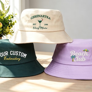 Può includere: Tre cappelli a secchiello color crema, verde scuro e lavanda. Il cappello color crema ha il testo "GERENARTRA" e "Cherry Martini". Il cappello verde dice "YOUR CUSTOM Embroidery". Il cappello lavanda dice "Beach Club" con una palma e un ombrellone.